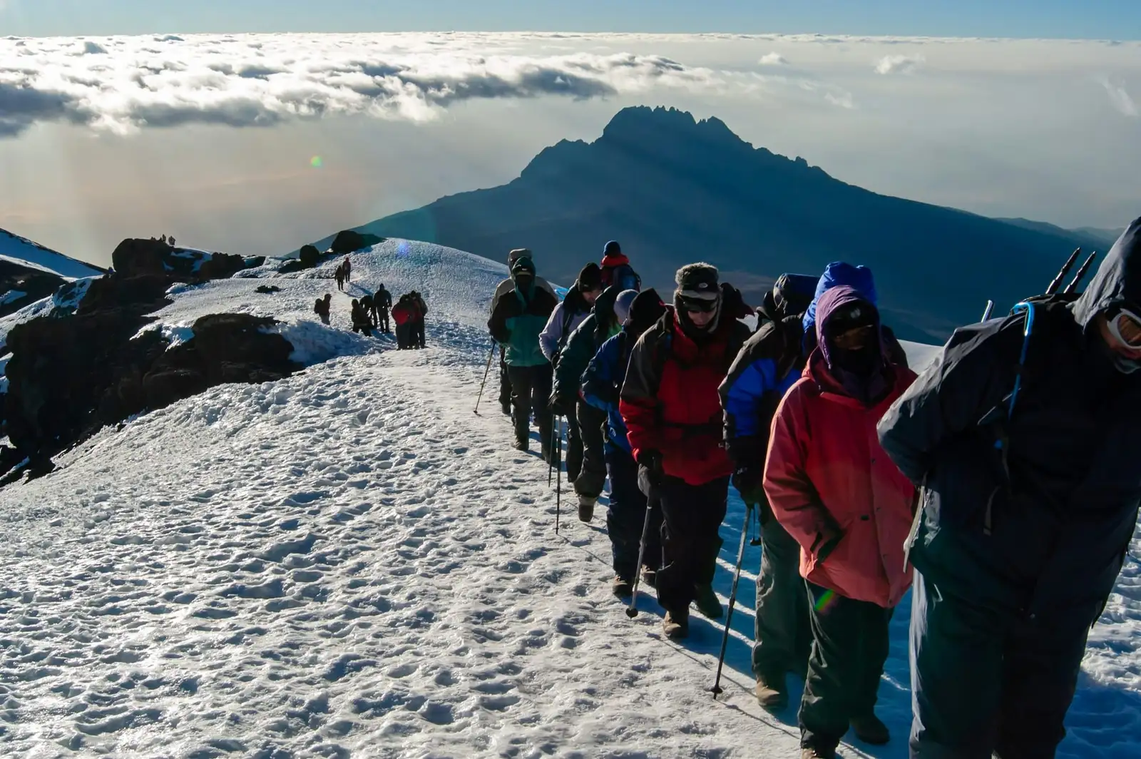 Wspinacze na zaśnieżonym grzbiecie pod Uhuru Peak, w tle szczyt Mawenzi nad chmurami