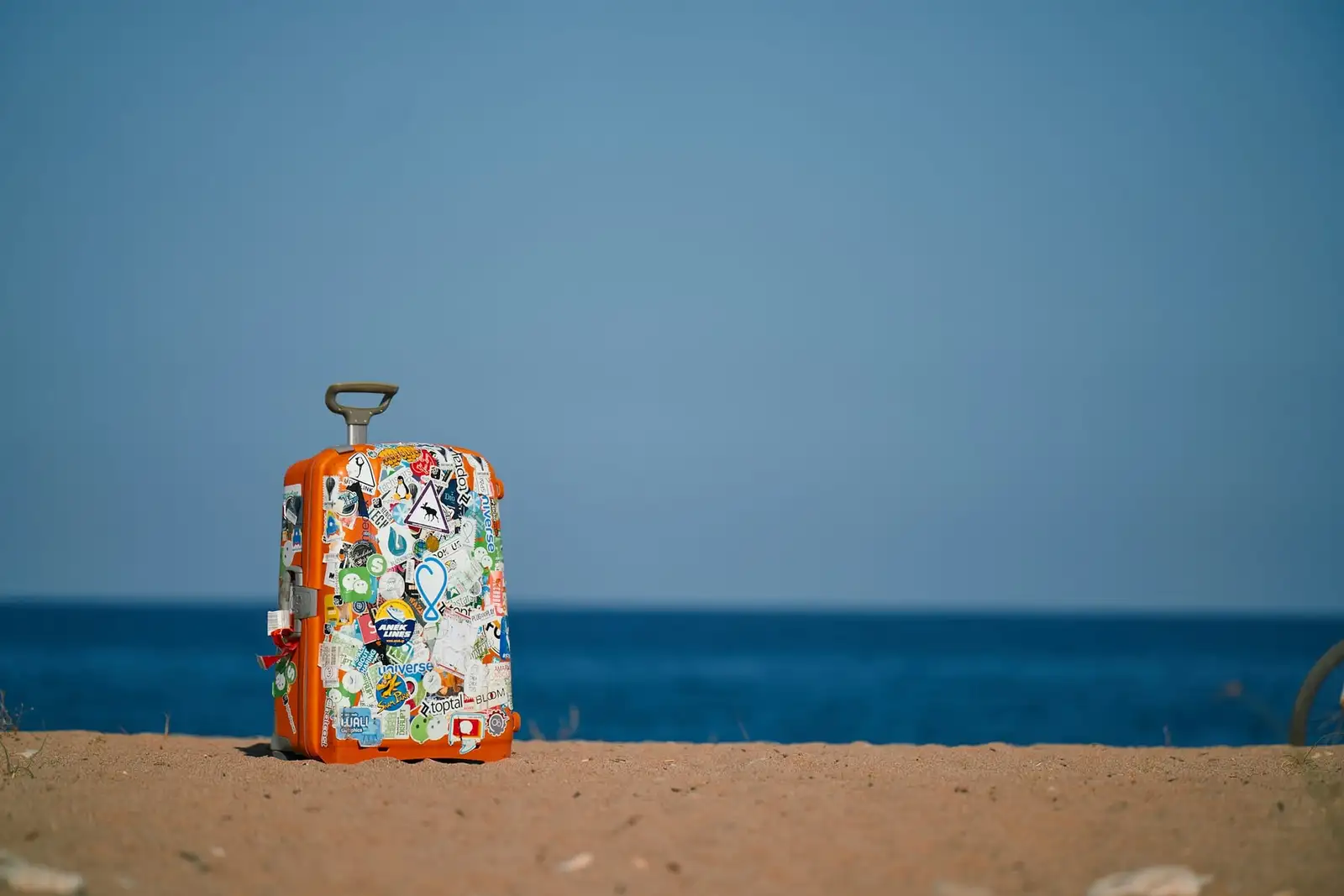 Walizka z naklejkami na piaszczystej plaży nad morzem